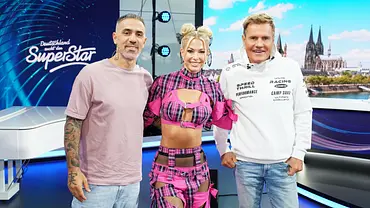 Die DSDS-Jurymitglieder stehen gemeinsam im Studio vor dem „Deutschland sucht den Superstar“-Logo und einer Köln-Kulisse im Hintergrund. - Foto: RTL
