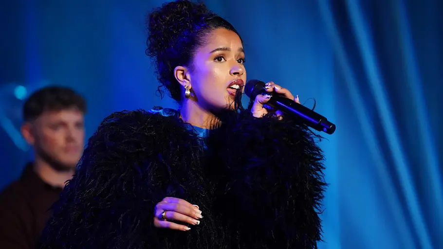 Noemi Stefaniak Noemi mit lockigem Haar und schwarzem, auffälligem Oberteil singt ins Mikrofon.