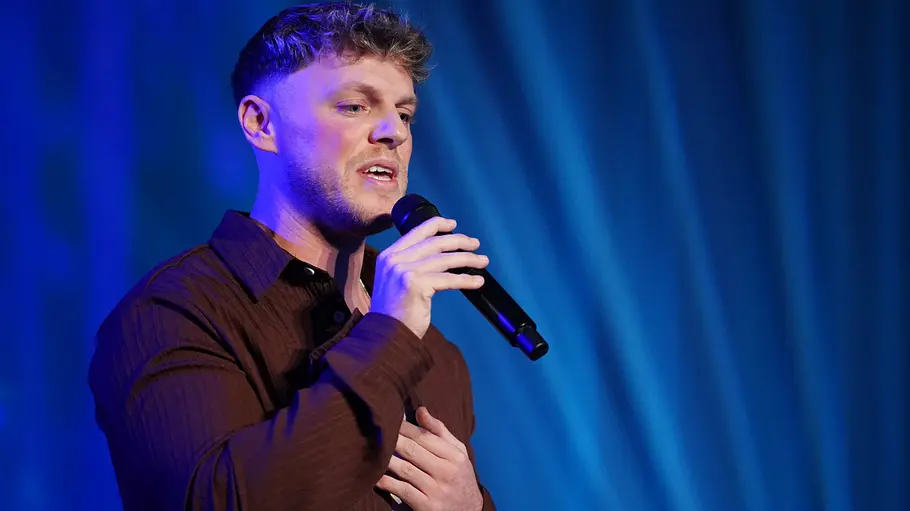 Maric Verch Maric mit braunem Hemd singt gefühlvoll ins Mikrofon, eine Hand auf der Brust, Bühnenlicht in Blau.