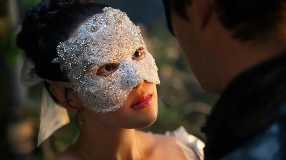 Sophie schaut Benedict an. Beide tragen eine Maske und wissen in diesem Moment nichts von der Identität des anderen.