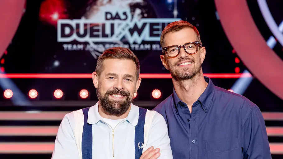 Duell um die Welt mit Joko und Klaas Links Klaas Heufer-Umlauf, rechts daneben Joko Winterscheidt grinsend vor dem Das Duell um die Welt-Logo
