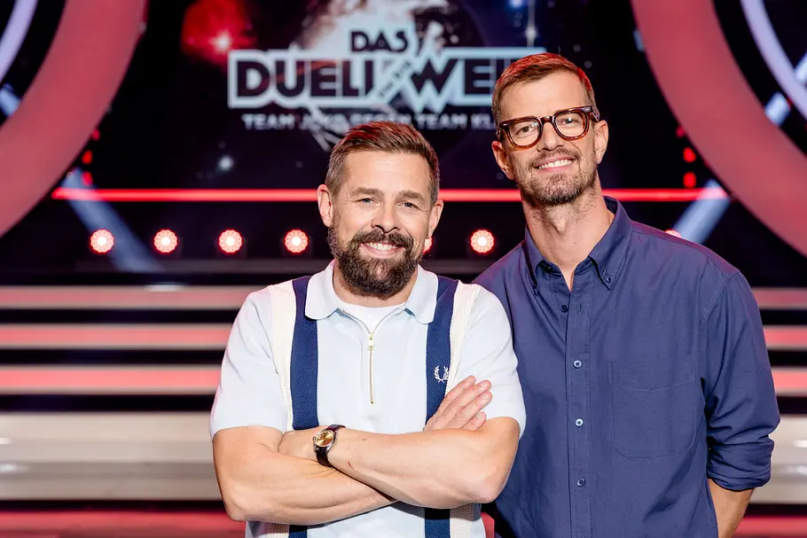 Links Klaas Heufer-Umlauf, rechts daneben Joko Winterscheidt grinsend vor dem Das Duell um die Welt-Logo