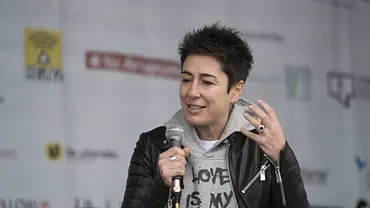 Dunja Hayali hält ein Mikrofon und gestikuliert mit erhobener Hand. Sie trägt eine schwarze Lederjacke über einem grauen Hoodie. - Foto: IMAGO / ecomedia/robert fishman Dunja Hayali hält ein Mikrofon und gestikuliert mit erhobener Hand. Sie trägt eine schwarze Lederjacke über einem grauen Hoodie. - Foto: IMAGO / ecomedia/robert fishman