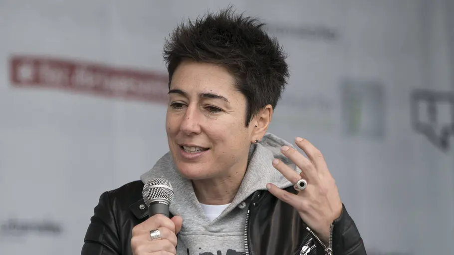 Dunja Hayali zu AfD-Verbotsverfahren Dunja Hayali hält ein Mikrofon und gestikuliert mit erhobener Hand. Sie trägt eine schwarze Lederjacke über einem grauen Hoodie.