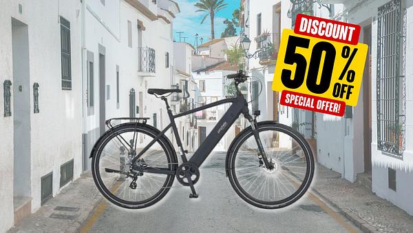E-Bike vor einer sommerlichen Kleinstadt und einem 50%-Rabatt-Preisschild - Foto: TVM/PR