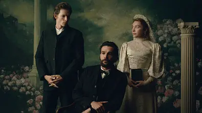 Chalres steht in East of Eden im dunkle Anzug neben seinem Bruder Adam und dessen Frau Cahty, die im Brautkleid zu ihm herüberschaut. - Foto: Netflix