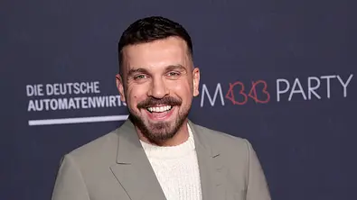 Edin Hasanovic steht vor einer Fotowand und lächelt sehr efreut.  - Foto: IMAGO / APress