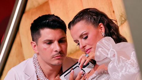 Patricija und Alexandru Ionel, beide in weißen Outfits mit Perlenbesatz, schauen am Rande von „Let’s Dance“ auf ein Handy - Foto:  IMAGO / Panama Pictures