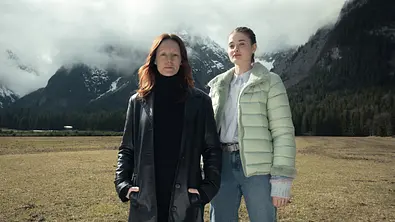 “Der Garmisch-Krimi - Wolfsmord“: Ira Zach (Lavinia Wilson) und Daphne Meindl (Philine Schmölzer) stehen auf einer Wiese in Garmisch vor hohen Bergen, deren Gipfel der Nebel bedeckt. - Foto: ZDF / Linda Gschwentner