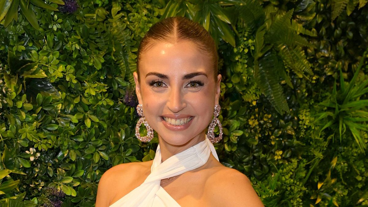 Ekaterina Leonova trägt große, hängende Ohrringe und ein weißes Kleid. Sie strahlt glücklich in die Kamera.