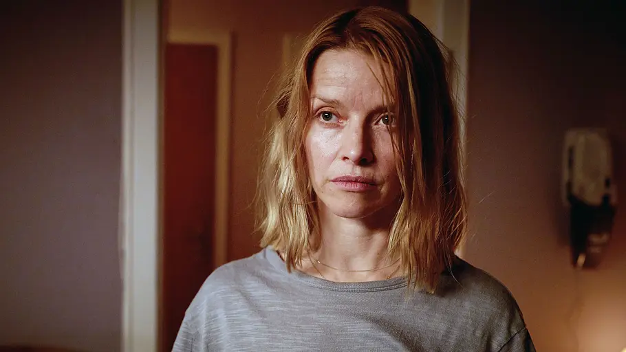 Karoline Schuch Elodie Karoline Schuch mit schulterlangen blonden Haaren und grauem T-Shirt blickt ernst zur Seite. Hinter ihr hängt ein Wandtelefon.