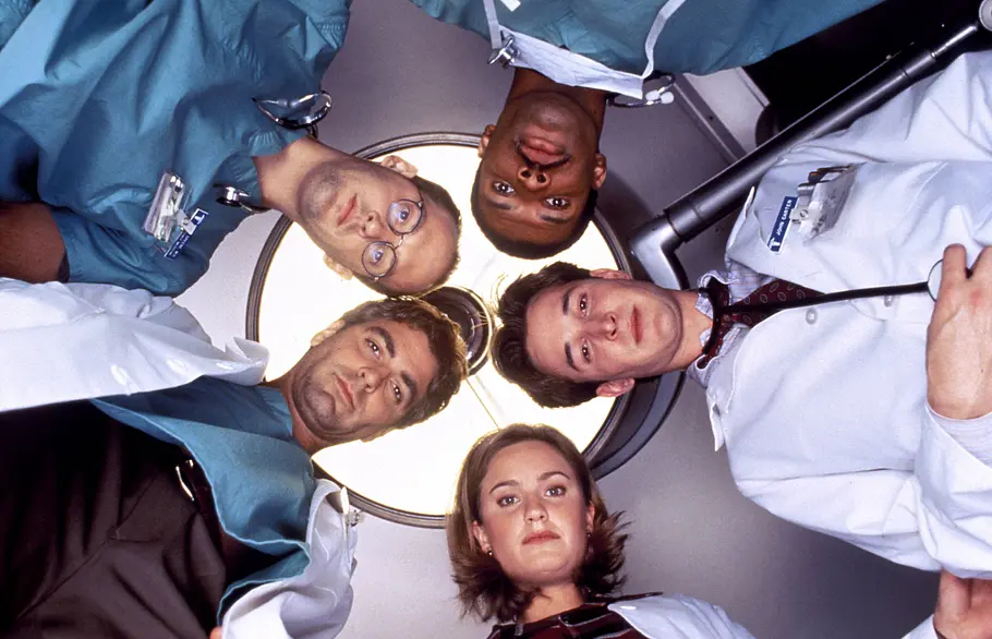 Der „Emergency Room“-Cast in Arztkleidung beugt sich aus der Perspektive eines Patienten über die Kamera.