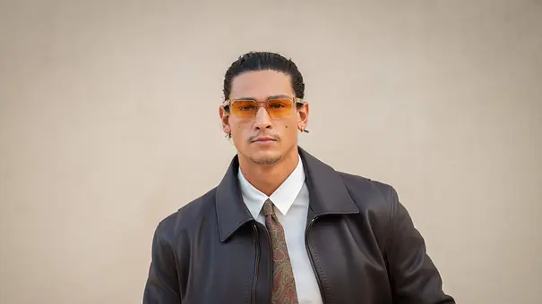 Emilio Sakraya trägt eine orange getönte Brille, eine dunkle Lederjacke, ein weißes Hemd und eine gemusterte Krawatte. - Foto: IMAGO / ABACAPRESS