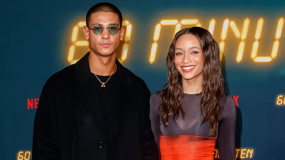 Emilio Sakraya im schwarzen Mantel und Jenny Augusta im grau-orangen Kleid posieren vor einer „60 Minuten“-Fotowand.