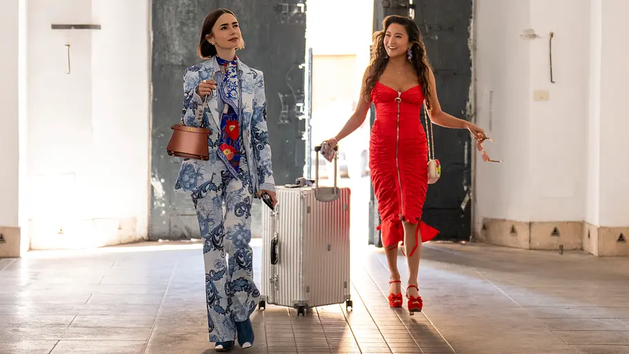 Emily (Lily Collins) und Mindy (Ashley Park) laufen in schicker Kleidung einen Innenhof entlang. Mindy zieht einen Koffer.