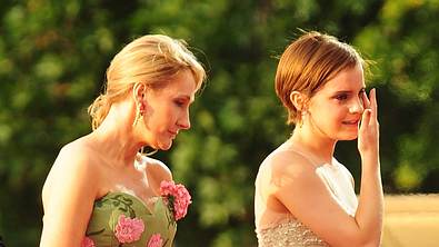 Auf dem Foto ist links J.K. Rowling zu sehen. Sie trägt ein grünes, schulterfreies Kleid mit pinkfarbenen Blumenapplikationen und goldenen Ohrringen. Ihr blondes Haar ist nach hinten gebunden. Rechts neben ihr steht Emma Watson in einem hellen, glitzernden Kleid mit feinen Trägern. Sie hat eine Hand an ihrem Gesicht, als würde sie sich eine Träne abwischen oder ist sichtlich bewegt. - Foto: IMAGO / Avalon.red