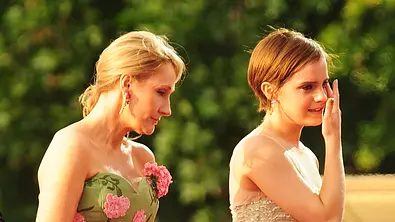 Auf dem Foto ist links J.K. Rowling zu sehen. Sie trägt ein grünes, schulterfreies Kleid mit pinkfarbenen Blumenapplikationen und goldenen Ohrringen. Ihr blondes Haar ist nach hinten gebunden. Rechts neben ihr steht Emma Watson in einem hellen, glitzernden Kleid mit feinen Trägern. Sie hat eine Hand an ihrem Gesicht, als würde sie sich eine Träne abwischen oder ist sichtlich bewegt. - Foto: IMAGO / Avalon.red