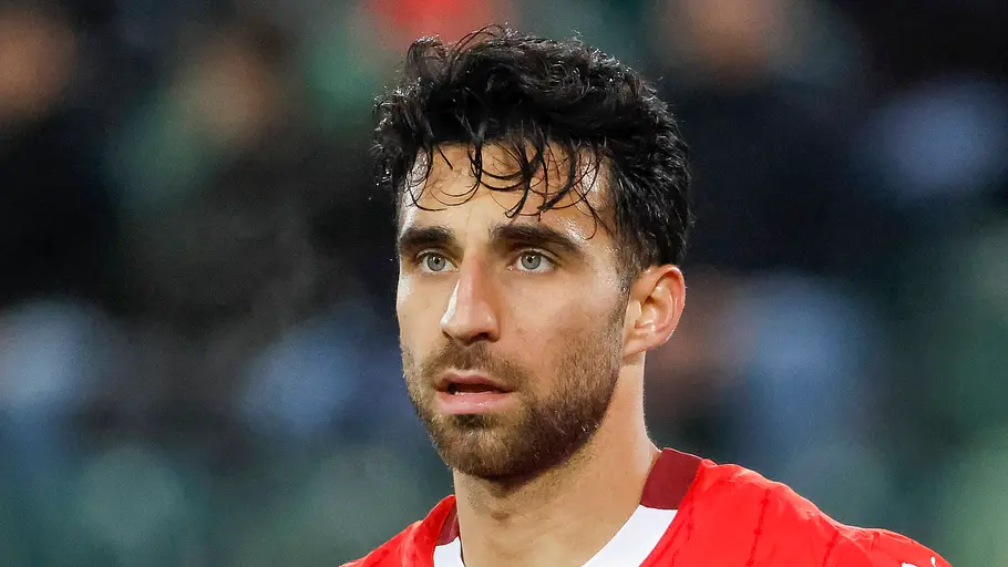 Nahaufnahme eines Fußballspielers im roten Trikot der Schweizer Nationalmannschaft. Mit nassen Haaren und konzentriertem Blick steht er während eines Spiels auf dem Platz, der Hintergrund des Stadions ist unscharf.