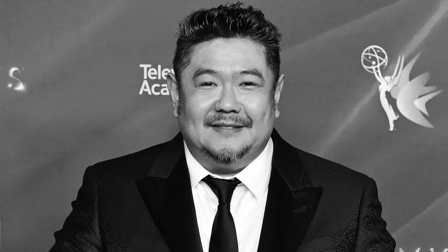 Eric Bauza (†46) ist tot Eric Bauza posiert im dunklen Anzug mit ausgebreiteten Armen vor einer Emmy-Logowand. Die Aufnahme ist schwarz-weiß.