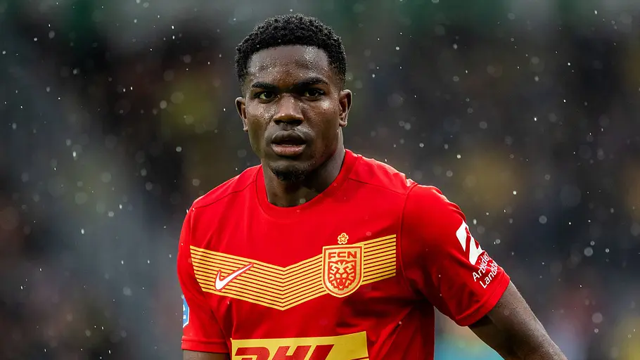 Fußballspieler des FC Nordsjælland im roten Trikot während eines Spiels. Im Regen blickt er konzentriert nach vorne, der Hintergrund des Stadions ist unscharf.