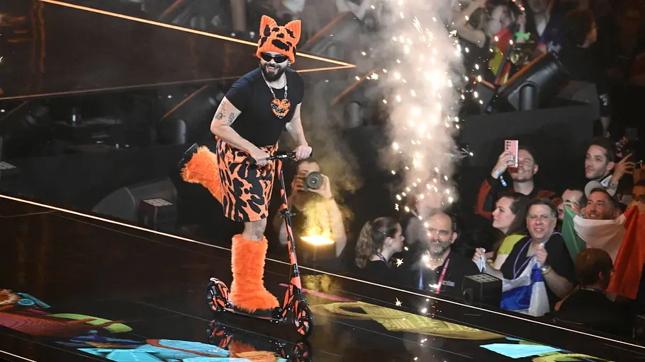 ESC 2026 Akylas Akylas fährt mit einem Roller über die Bühne. Er trägt Kleidung in Tiger-Optik.