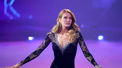Esther Schweins steht an einer Barre, sie trägt ein schwarzes Kleid mit Spitze und blickt ernst. - Foto: IMAGO / Panama Pictures