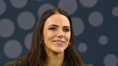 Esther Sedlaczek, Moderatorin von „Quizduell-Olymp“, lächelt vor einem dunklen Hintergrund. - Foto: IMAGO / Sven Simon