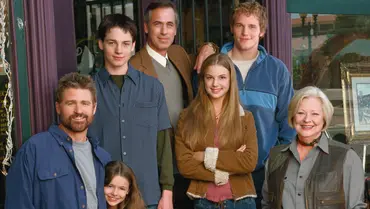 Die Hauptcharaktere der Serie „Everwood“: Gruppenfoto mehrerer Schauspieler und Schauspielerinnen vor einem Schaufenster; die Personen stehen nah beieinander, lächeln in die Kamera und tragen legere Alltagskleidung. Im Hintergrund sind Bilderrahmen und Gegenstände in einem Schaufenster zu erkennen. - Foto: Warner Bros.