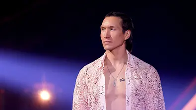 Evgeny Vinokurov steht im Rampenlicht und schaut mit ernster Miene zur Seite. Er trägt ein offenes Spitzen-Hemd. - Foto:  IMAGO / Panama Pictures