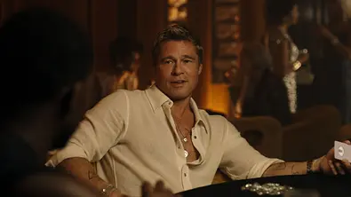 Man sieht Brad Pitt in einem weißen Hemd. Er sitzt an einem Tisch und hat eine Spielkarte in der Hand. Das Licht ist stimmungsvoll gedimmt. - Foto:  IMAGO / ZUMA Press