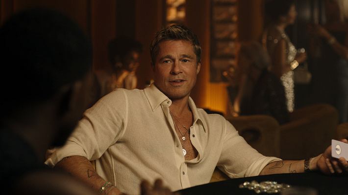 Man sieht Brad Pitt in einem weißen Hemd. Er sitzt an einem Tisch und hat eine Spielkarte in der Hand. Das Licht ist stimmungsvoll gedimmt. - Foto:  IMAGO / ZUMA Press