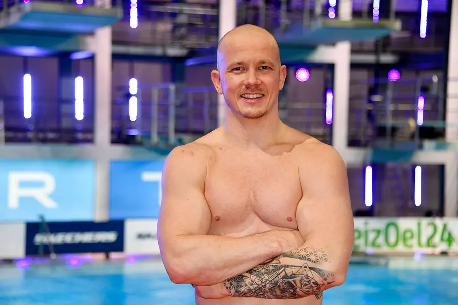Fabian Hambüchen mit freiem Oberkörper und verschränkten Armen in einer Schwimmhalle