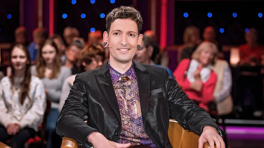 Fabian Kahl Fabian Kahl sitzt lächelnd auf einem Stuhl bei einer Talkshow.