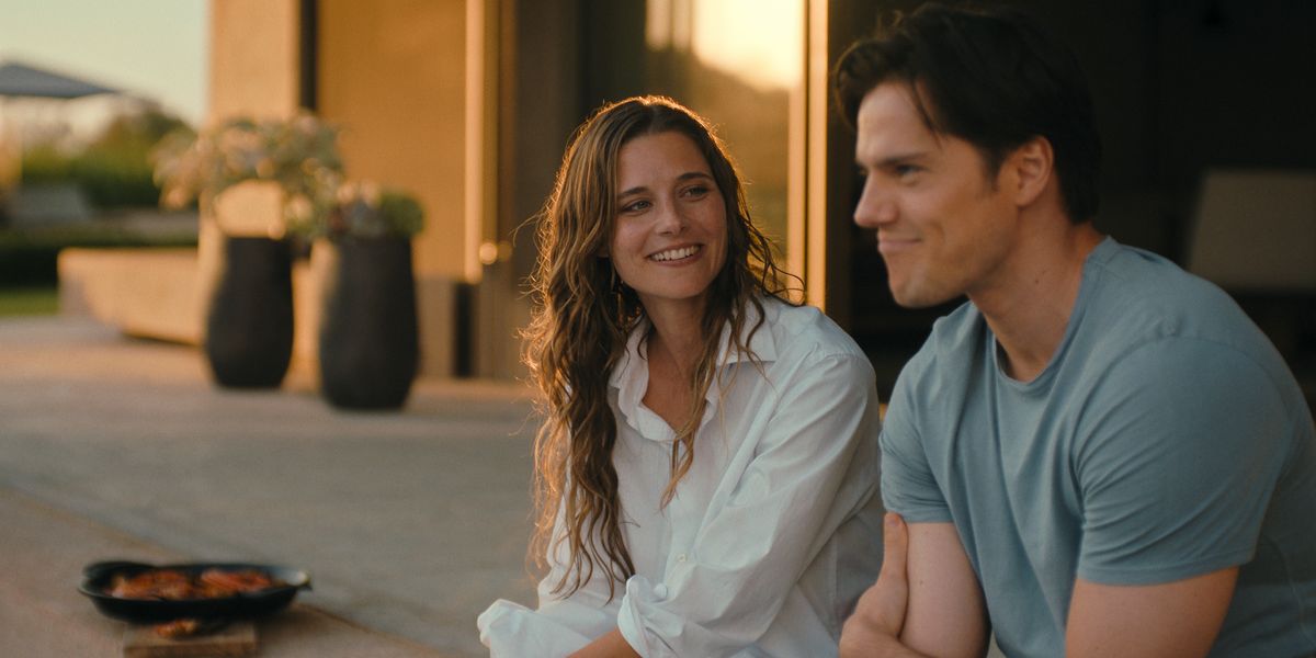 Lilli (Svenja Jung) und Tom (Theo Trebs) sitzen entspannt nebeneinander im warmen Abendlicht. Sie lächelt ihn an, während er gedankenverloren nach vorne blickt. Im Hintergrund sind Pflanzen und die Terrasse eines modernen Hauses zu sehen.