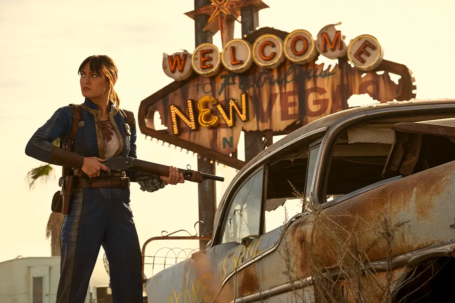 Lucy in Fallout Season 2 Ella Purnell steht vor dem Welcome to New Vegas Logo mit einer Schrottflinte in der Hand
