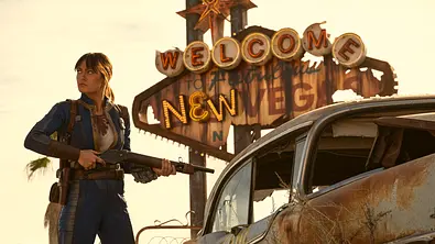 Lucy (Ella Purnell) steht mit Schrottflinte in der Hand vor dem Welcome to New Vegas Schirftzug - Foto: Prime Video
