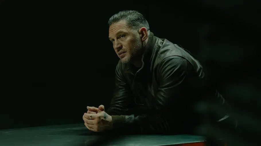 Fans sehen Tom Hardy sehr gerne, nur Dreharbeiten mit ihm sind wohl schwierig. Tom Hardy lehnt sich über einen Tisch.
