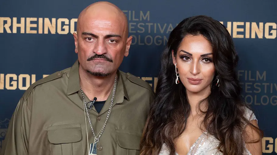 Xatar und seine Ehefrau Farvah Hajabi Xatar und Farvah: Beide blicken ernst in die Kamera und stehen vor einer Fotowand mit goldener Schrift beim Film Festival Cologne.