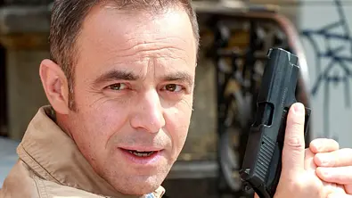 Felix Eitner schaut mit direktem Blick in die Kamera, während er eine Waffe hoch hält. - Foto: IMAGO / STAR-MEDIA