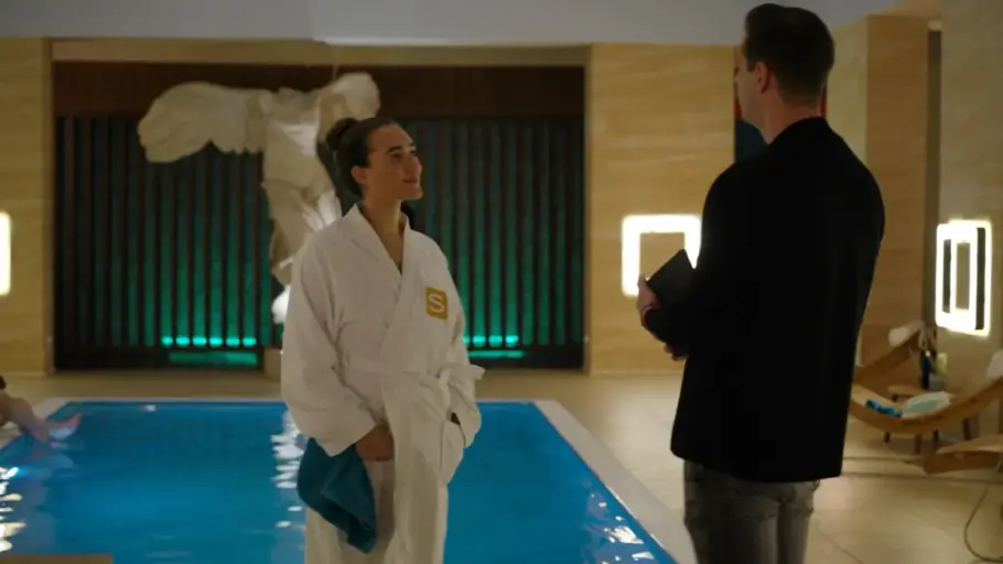 Joana im Bademantel und Deniz stehen vor dem Pool im Wellnesscenter