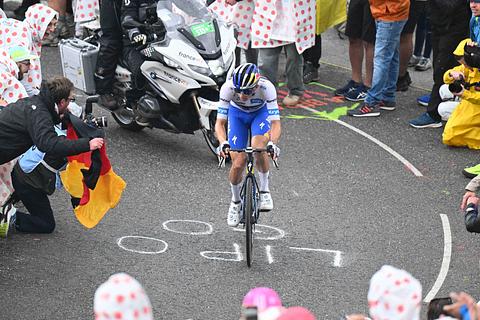 Florian Lipowitz fährt den Berg bei der 18. Etappe der Tour de France hoch und wird von Fans mit Deutschland-Fahne umzingelt. - Foto: IMAGO / Sirotti