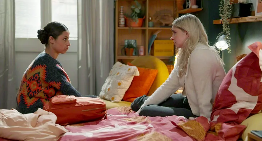 Elli und Toni Rote Rosen Elli und Toni sitzen sich auf einem Bett gegenüber und sehen einander ernst an. Zwischen ihnen liegt eine orangefarbene Tasche.
