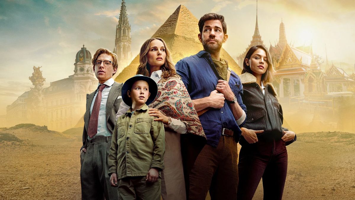 John Krasinski ist bald ein letztes Mal als Jack Ryan zu sehen. Die besetzung aus „Fountain of Youth“ steht in der Wüste. Hinter ihnen sind diverse Sehenswürdigkeiten aus diversen Ländern zu sehen.