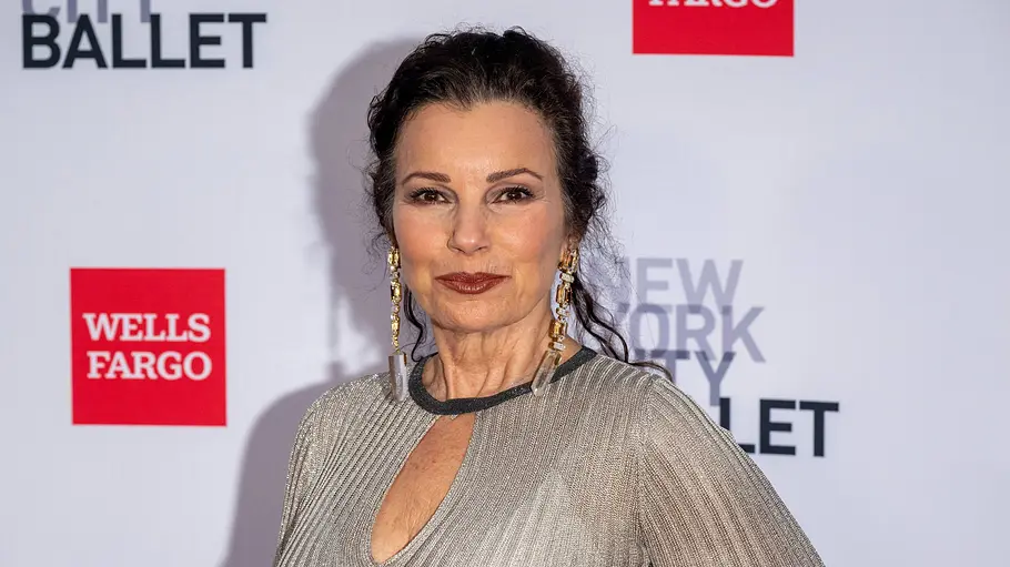 Fran Drescher trägt ein silberfarbenes Kleid und lange Ohrringe vor einer Logowand des New York City Ballet und Wells Fargo.