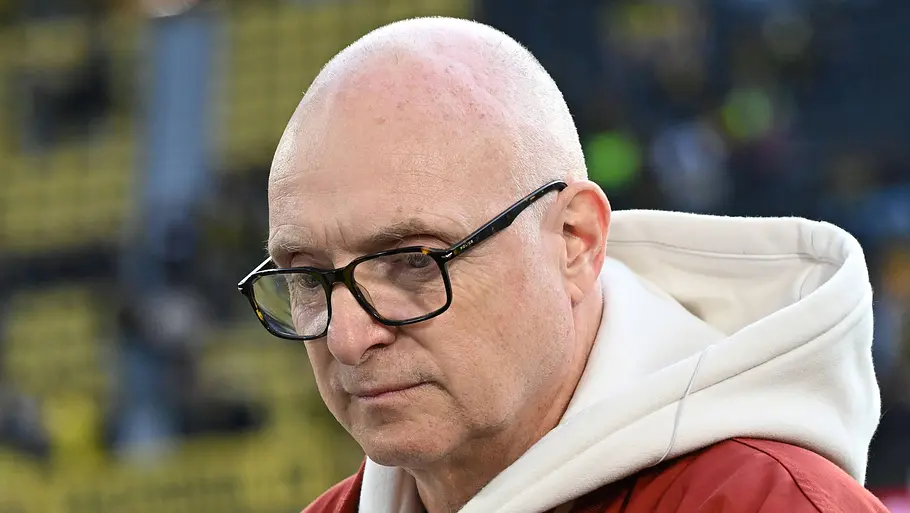 Frank Buschmann hat eine Entscheidung getroffen. Frank Buschmann trägt eine Brille, einen weißen Hoodie und eine rote Jacke. Er blickt ernst nach unten.