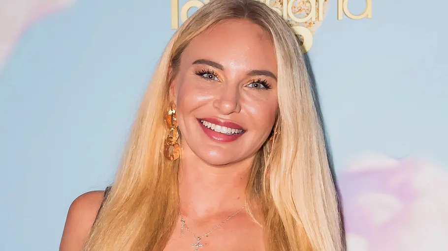 Franziska Temme: Eine lächelnde Frau mit langen blonden Haaren trägt ein schwarzes Spitzenoutfit vor einer Wand mit „Love Island VIP“-Logos.