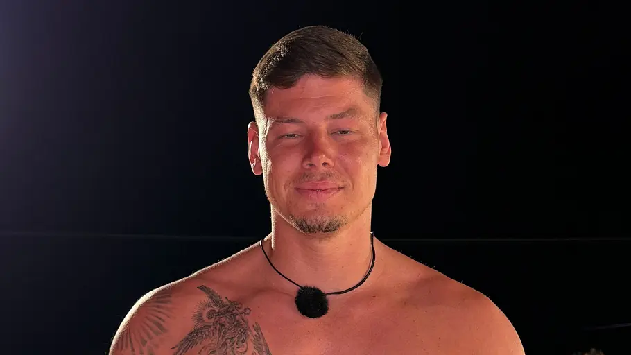 Frederik, 29 Ein Mann mit freiem Oberkörper, Tattoos und einem Mikrofon am Hals steht nachts vor einem beleuchteten Pool.
