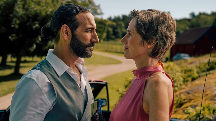 Frederika (Julia Bremermann) entdeckt, dass in dem Städtchen eine neue Tanzschule aufgemacht hat. Inga Lindström: Rezept für die Liebe: Frederika (Julia Bremermann) und Kian (Massimo Sinato) stehen im Freien dicht beieinander und sehen sich an. Im Hintergrund liegt eine sich schlängelnde Schotterstraße, umgeben von Bäumen und Wiese. Direkt hinter dem Paar steht ein rotes Cabrio mit offenem Dach.