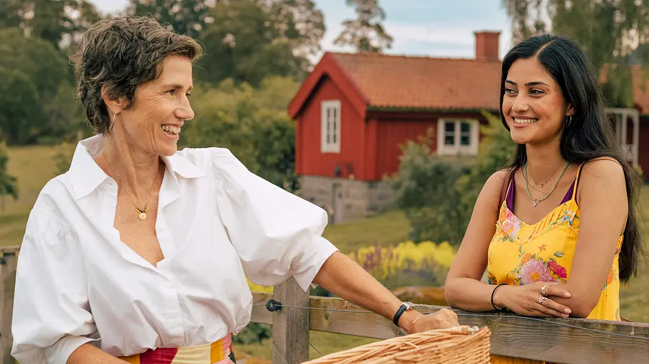 Frederika (Julia Bremermann, l.) begrüßt herzlich ihre einstige Nachbarin Sofia (Sogol Faghani, r.). Inga Lindström: Rezept für die Liebe: Sofia (Sogol Faghani) und Frederika (Julia Bremermann) stehen im Freien an einem Gartenzaun. Vor dem Zaun hält Frederika den Lenker eines Fahrrads. Hinter dem Zaun hat Sofia die Arme auf den Zaun gelegt. Die beiden Frauen sehen sich an und lachen.