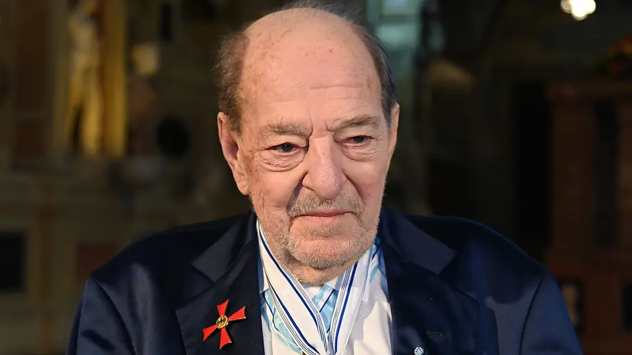 Freunde und Familienmitglieder sorgen sich um den Zustand von Ralph Siegel. Ralph Siegel trägt ein dunkelblaues Sakko mit rotem Orden am Revers und weitere Orden an weiß-blauen Bändern um den Hals.